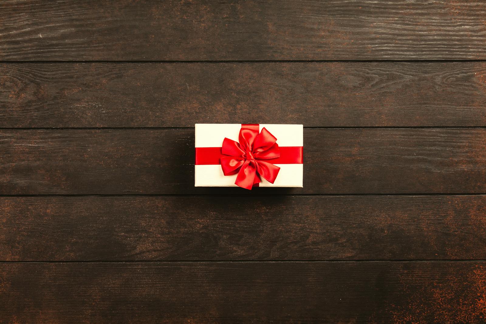Top view of a gift box with red ribbon on a dark wooden background, offering ample copyspace.